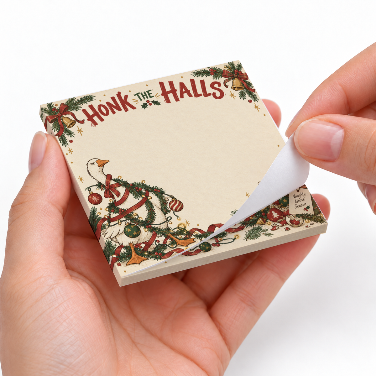 Hands peel a sheet from the Christmas goose sticky note pad, showing “Honk the Halls” and festive garland artwork.