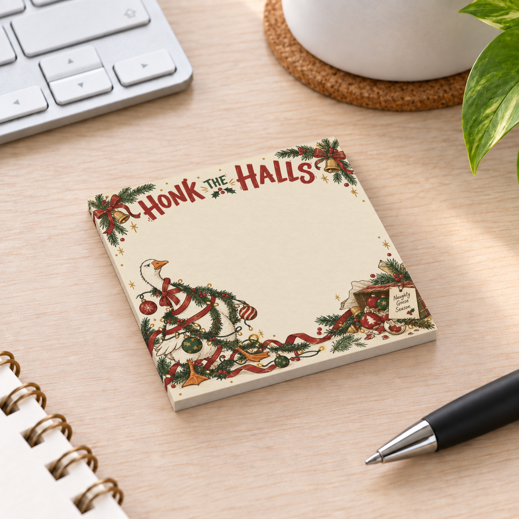 Honk the Halls Christmas goose sticky note pad sits on a wood desk beside a keyboard, pen, notebook, mug, and plant.
