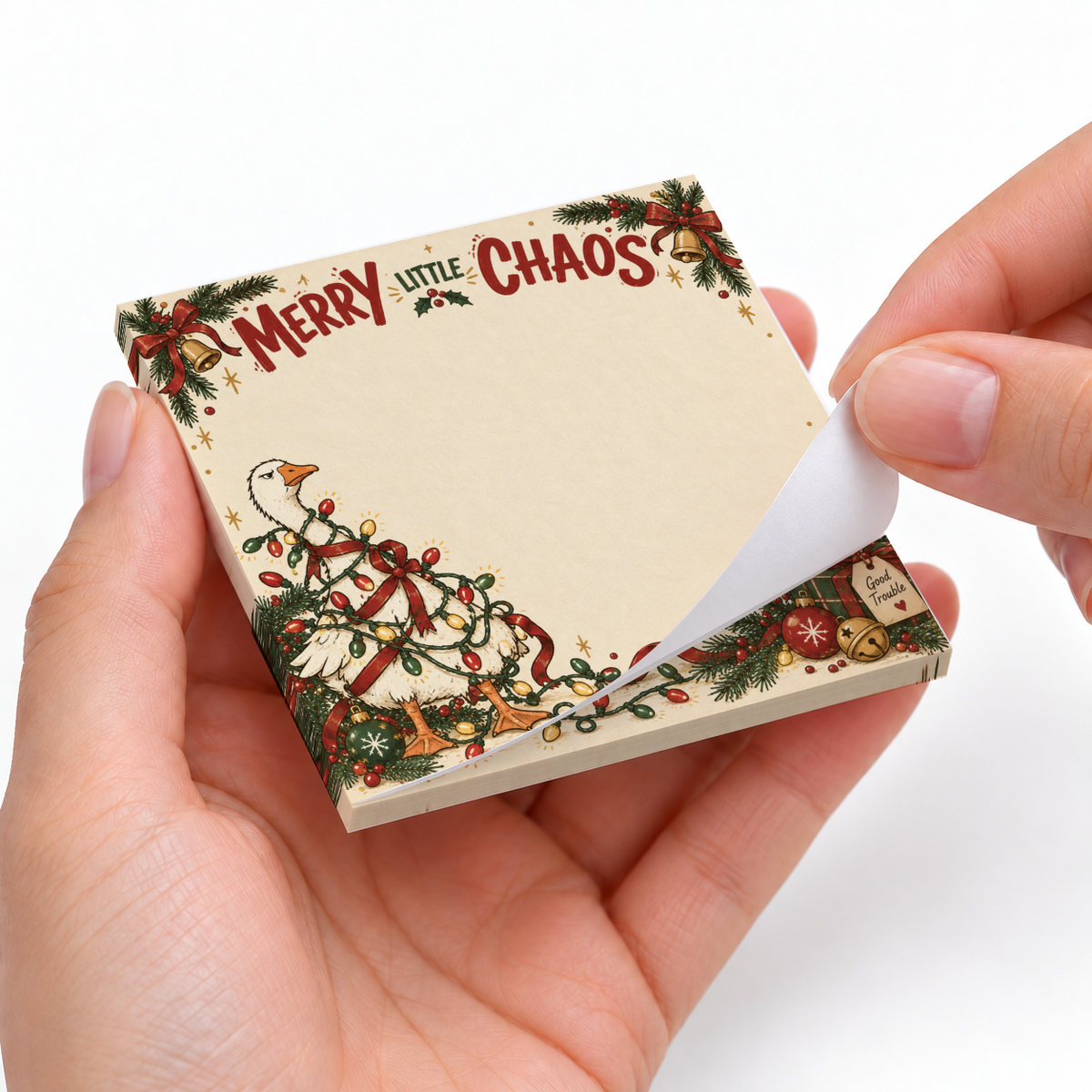 Hands peel a sheet from a Christmas goose sticky note pad with tangled lights and “Merry Little Chaos” text.