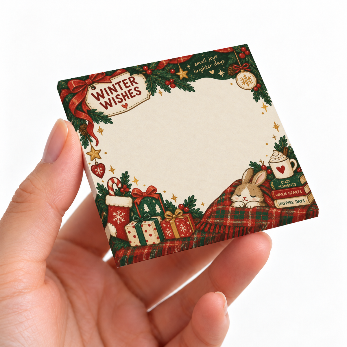 Hand holding a Winter Wishes sticky note pad with a bunny, plaid blanket, gifts, greenery, and ornaments.