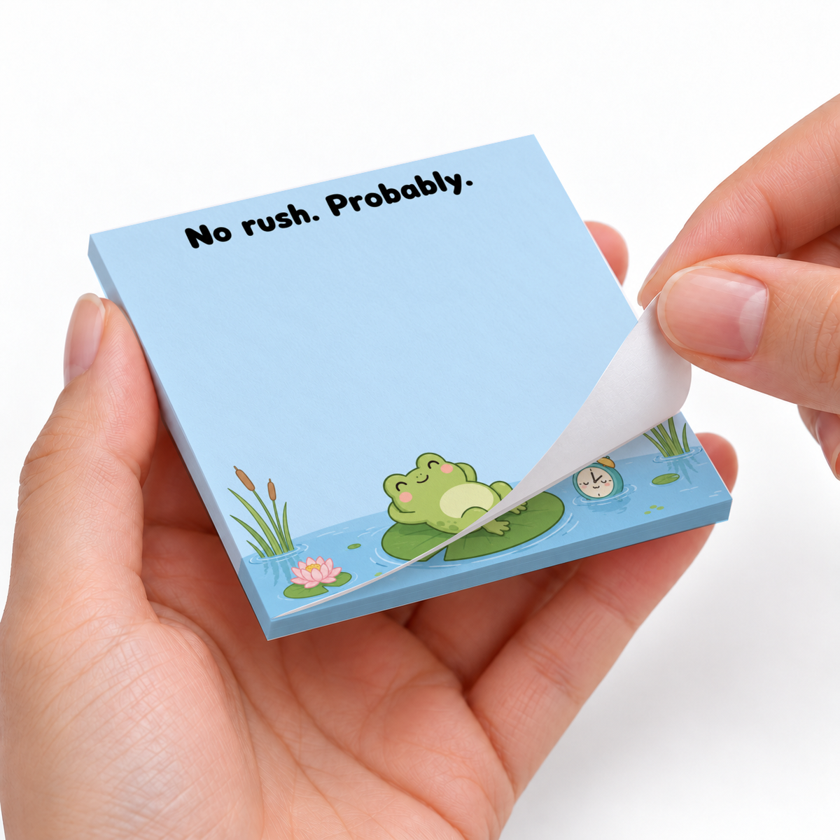 Hands peel a sheet from a blue frog sticky note pad featuring “No rush. Probably.” and a frog on a lily pad.