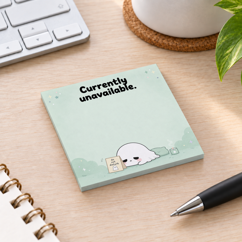 Sleepy Ghost sticky note pad reading “Currently unavailable” on a wood desk beside a keyboard, pen, and plant.