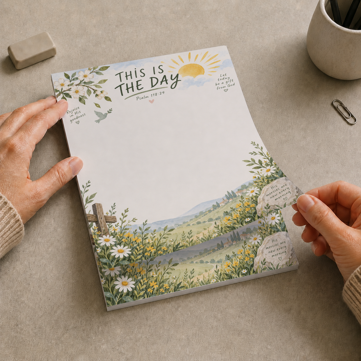Hands lifting a sheet from the This Is The Day Psalm 118 tear-off memo pad on a desk with an eraser and pen cup.