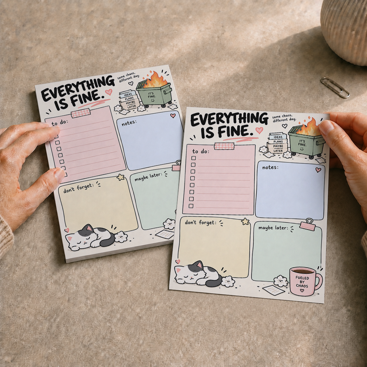 Hands holding one sheet of the Everything Is Fine Dumpster Fire Memo Pad next to the remaining stack on a speckled surface.