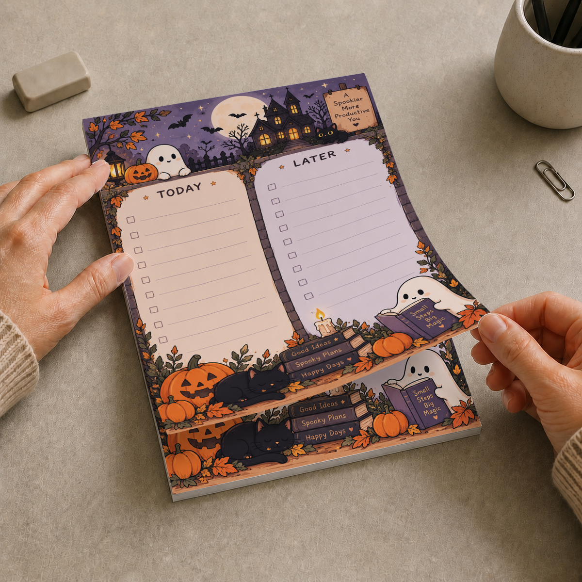 Hands lifting a sheet of a Spooky Haunted House Memo Pad on a desk, featuring checklists with ghosts and pumpkins.