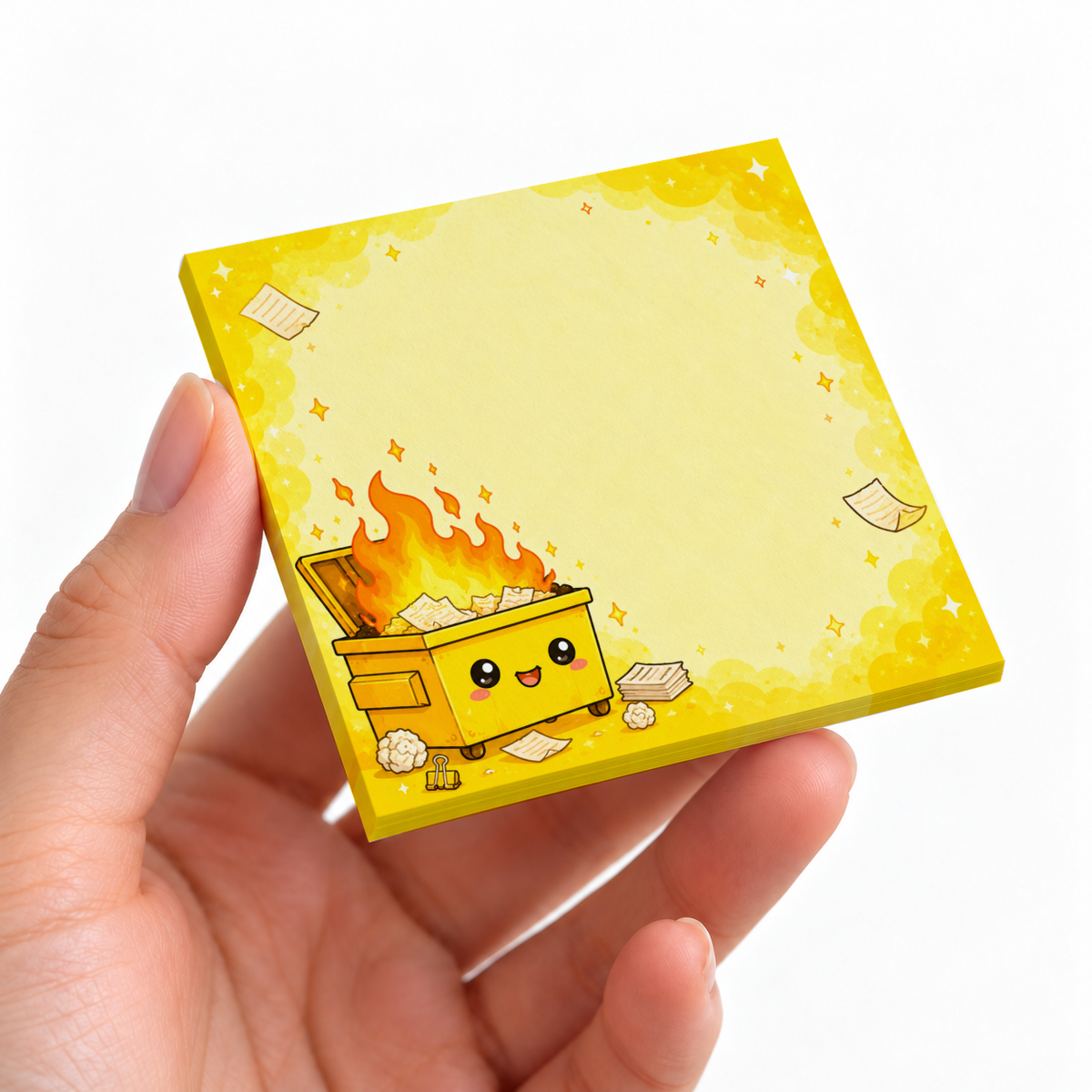 A hand holds a yellow sticky note pad with a smiling dumpster fire illustration and blank writing area.