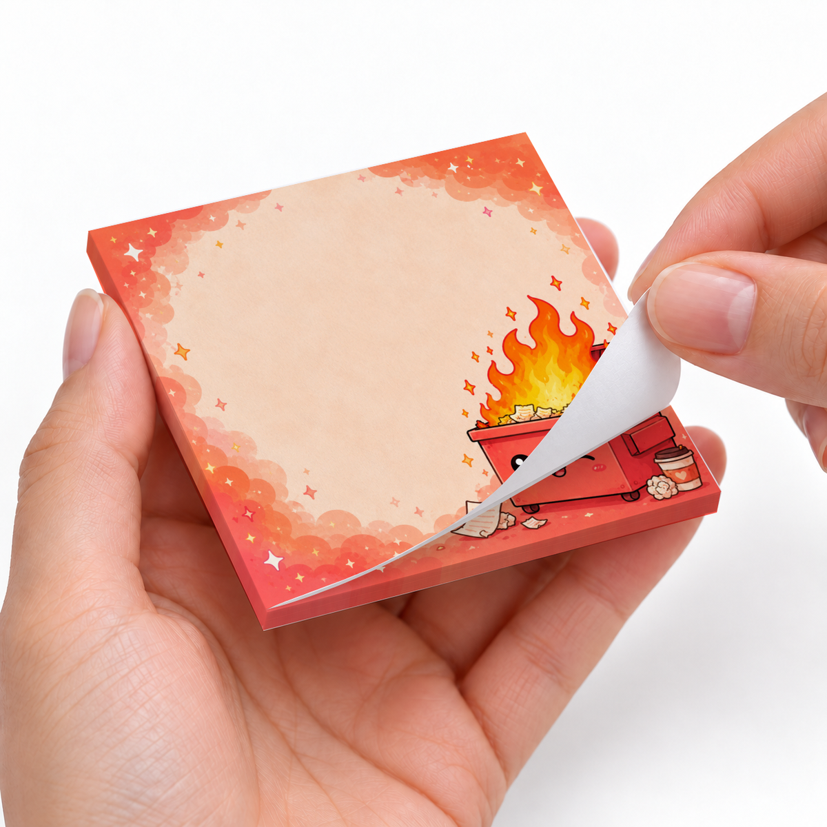 Hands peel back a sheet from the Dumpster Fire sticky note pad with a blank center and fiery red border.
