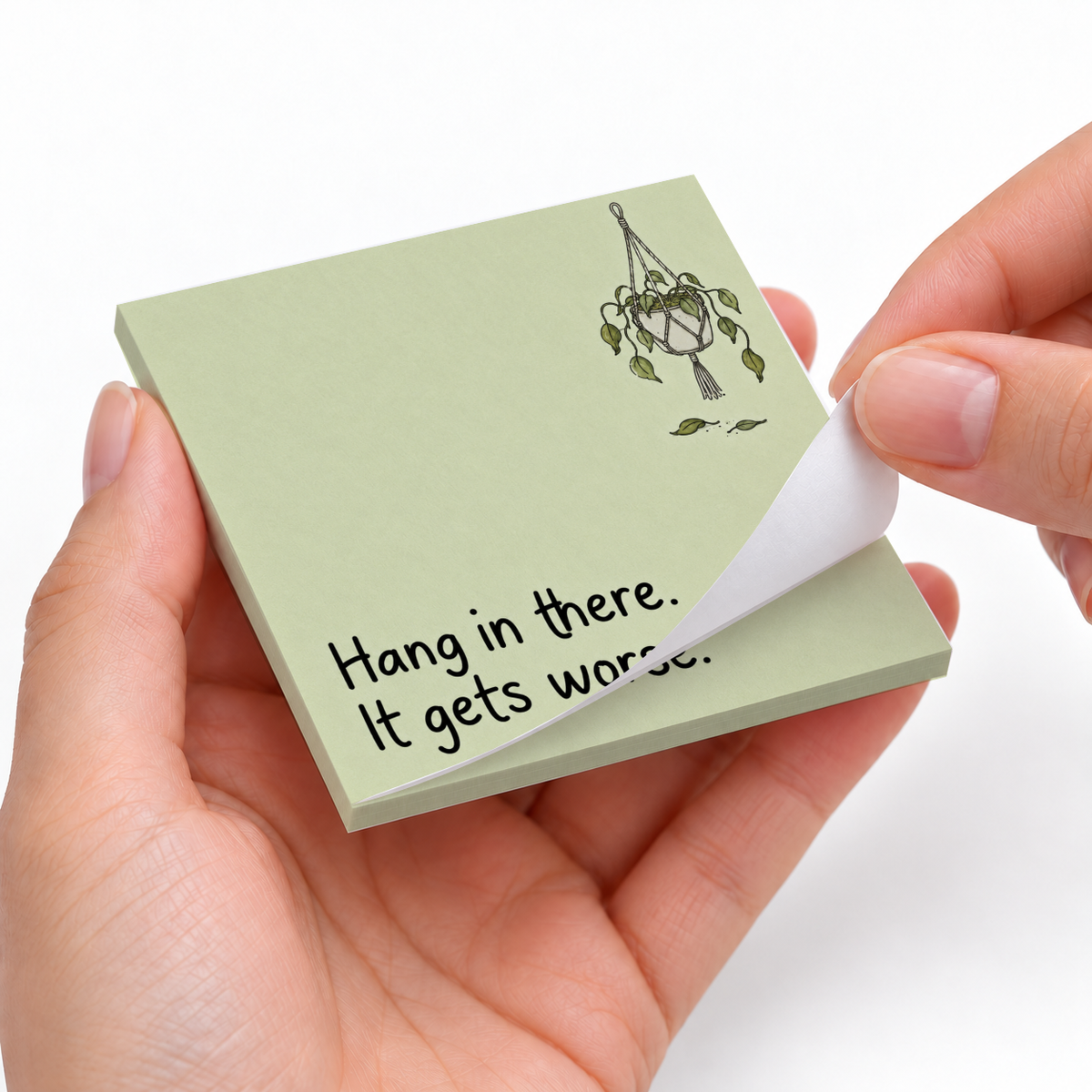 Hands peel a sheet from a pale green sticky note pad with a wilted plant and “Hang in there. It gets worse.”